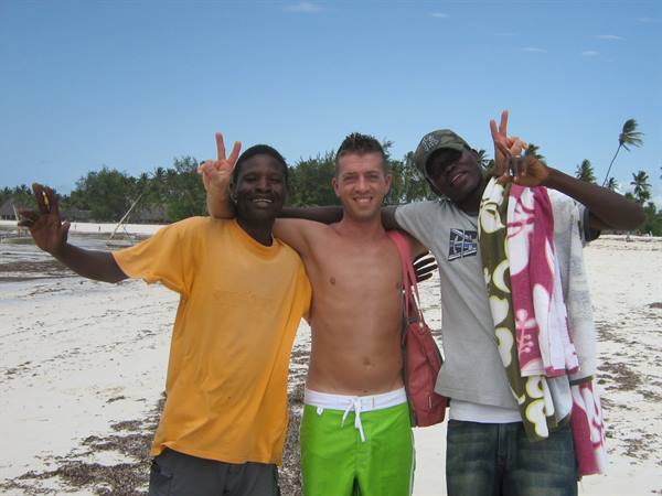 Three friends hugging and making peace signs on a white sand beach
