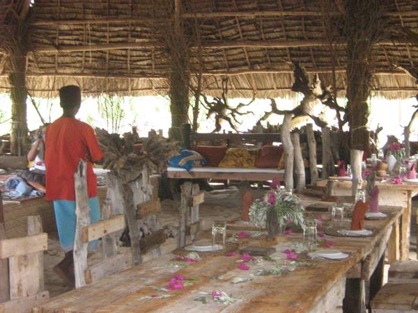 Wooden table with pink petals in a thatched-roof restaurant, a waiter in red