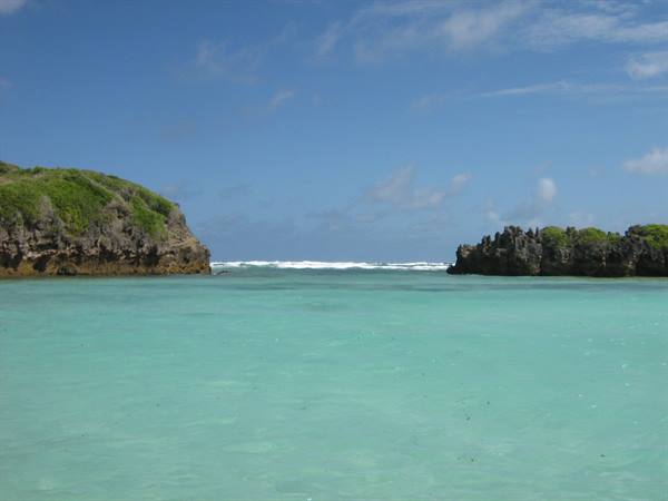 Turquoise water between green rocky cliffs, white waves on the horizon