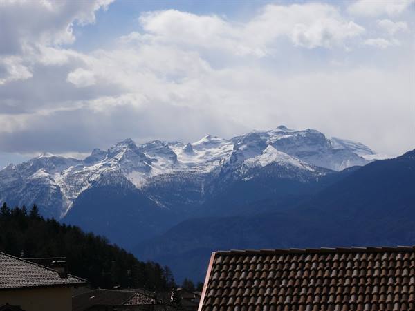 Tiled rooftops in front of snow-capped Dolomites under white clouds