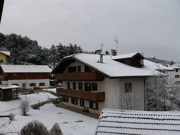 Alpine house with wooden balconies, snow-covered tiled roofs and snowy garden