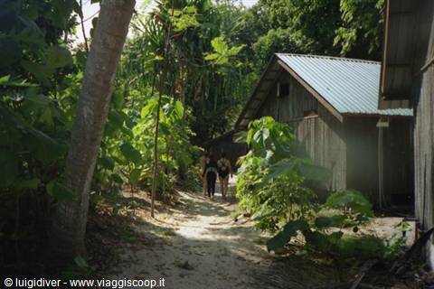 Women walk on sandy path between wooden houses with metal roofs