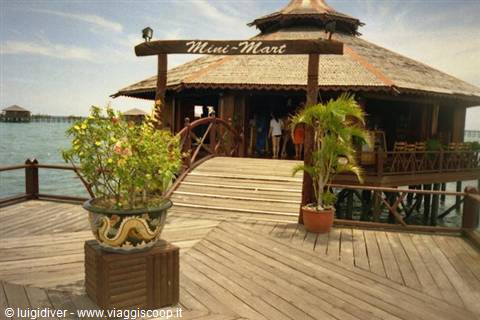 Wooden walkway with decorated pot toward stilt 'Mini-Mart' shop, daylight