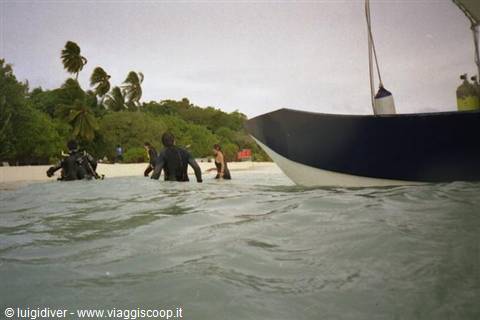 Divers in wetsuits enter the water beside a boat near a tropical beach