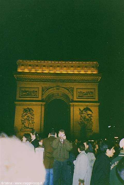 Tourists taking pictures beneath the illuminated Arc de Triomphe at night in Paris