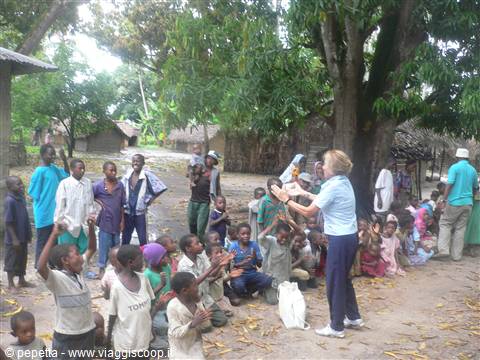 Blonde woman greets children sitting under a large tree in the village
