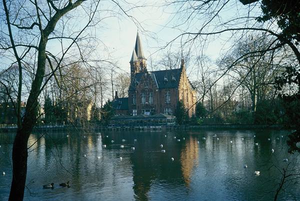 Minnewater lake in Bruges with swans, brick castle among bare trees
