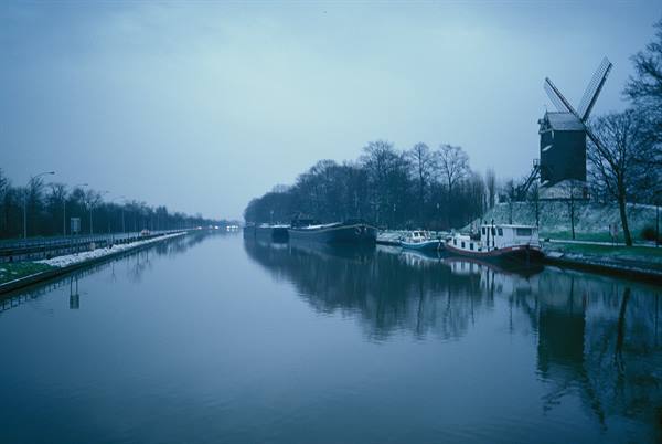 Brick windmill beside the canal with moored boats, misty light
