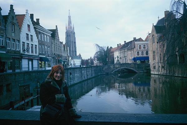 Girl on a bridge along a Bruges canal, medieval church and houses reflected in the water