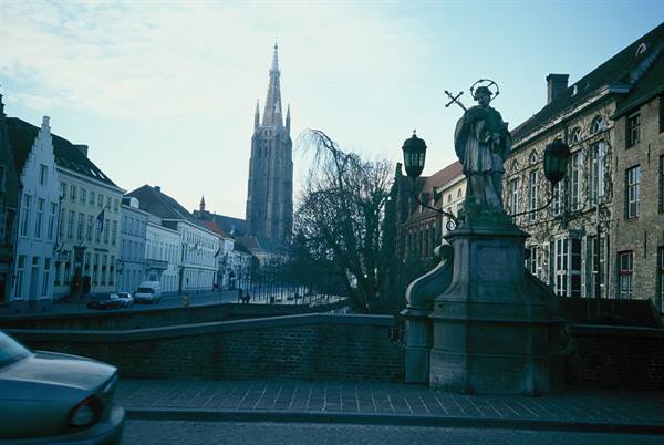 Saint statue on a stone bridge, canal and church spire in Bruges