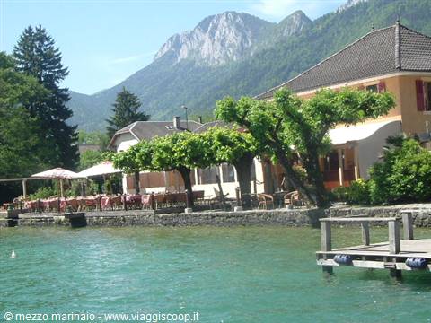 Lakeside restaurant with outdoor tables, wooden pier, green mountains behind