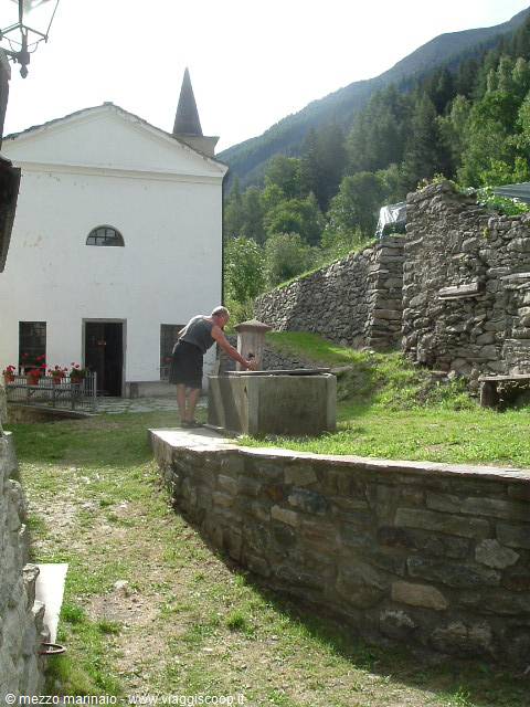 Man drawing water from stone fountain beside white mountain church