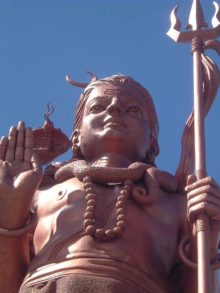Copper statue of Shiva holding a trident, snake around neck, against blue sky