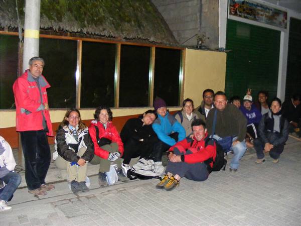 Group of travelers in red and blue jackets sitting at night outside a shop