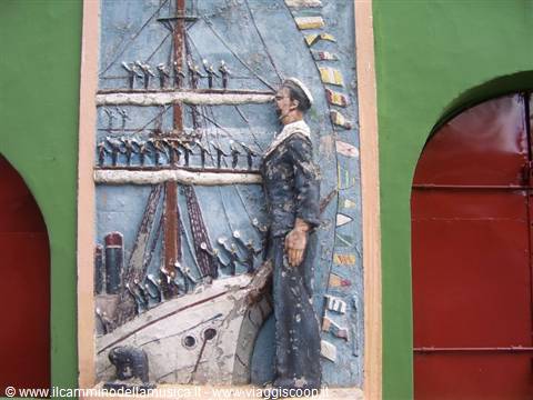Cement relief: sailor in uniform beside a crewed tall ship, green wall