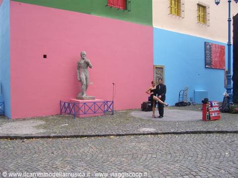 Tango dancers posing beside a statue among colorful houses in La Boca
