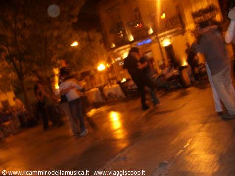 Couples dance tango at night on a stone square under golden lights