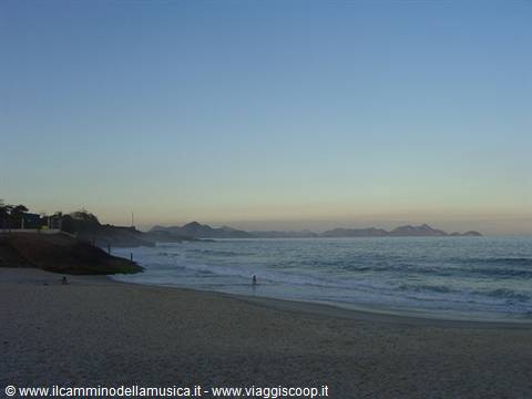 Sandy beach with waves and swimmers, mountains on the horizon at dusk