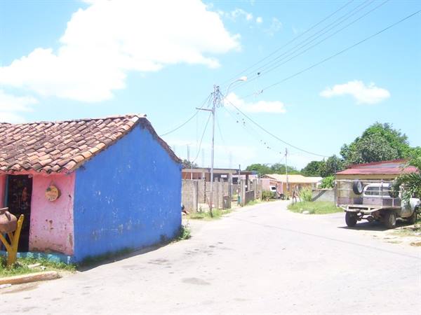 Colorful houses along village road, parked pickup truck, utility poles, cloudy sky