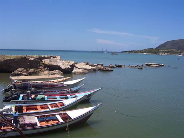 Colorful fishing boats moored near rocks, green bay with sunny mountains