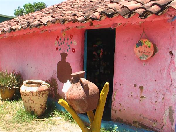 Pink house with clay tiles, terracotta amphora on yellow stand by entrance