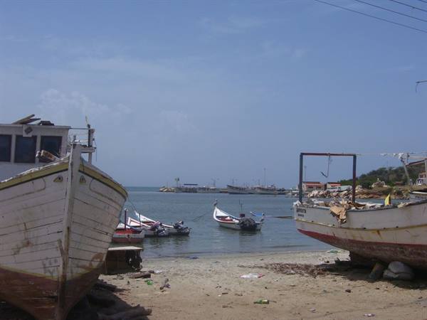 Wooden fishing boats beached on sand, others moored in the calm water
