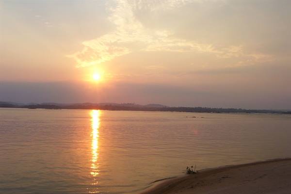 Low sun reflected on calm water in front of the sandy beach