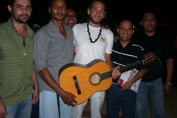 Group of smiling men at night, one holding a classical guitar