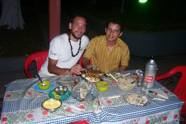 Two men dining outdoors with fish, rice and a rum bottle