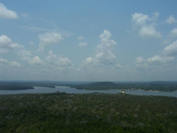 Green tropical forest before a wide lake, distant hills, cloudy blue sky