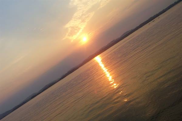 Low sun reflected on a wide lake, tree-lined shore in the distance