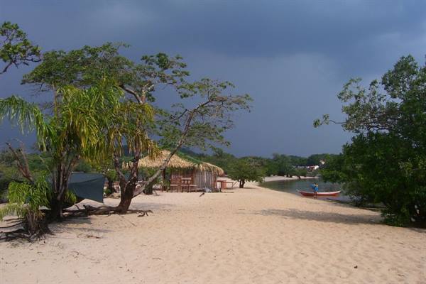Sandy beach with thatched hut and boat on shore, cloudy sky