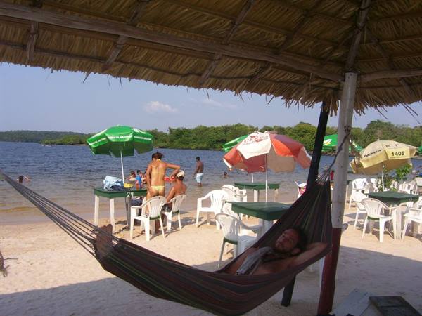 Man lying in hammock under thatched roof on beach with umbrellas