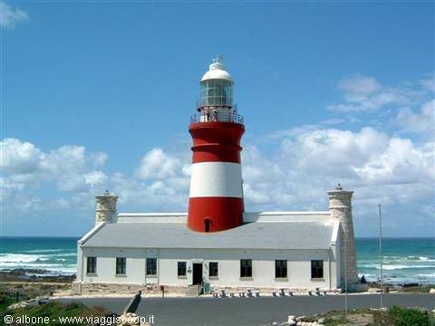 Red and white Cape Agulhas lighthouse in front of the ocean under cloudy sky