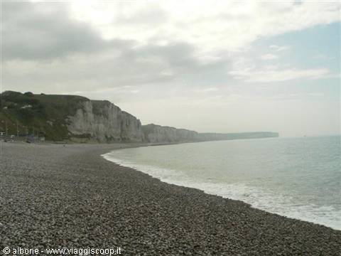 Pebble beach beneath white chalk cliffs, wave receding under cloudy sky