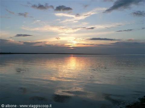 Low sun reflected on calm sea, golden clouds and dark shoreline