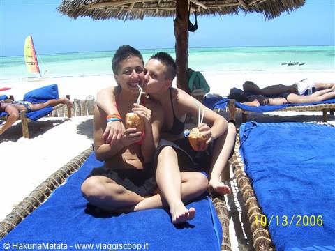 Two girls sipping coconut drinks under thatched shade on blue beach loungers