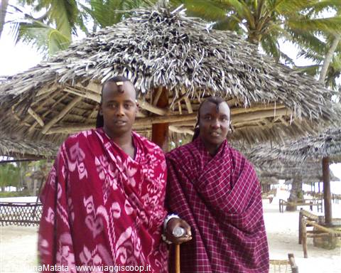 Two Maasai men in red shuka cloth under thatched beach umbrellas