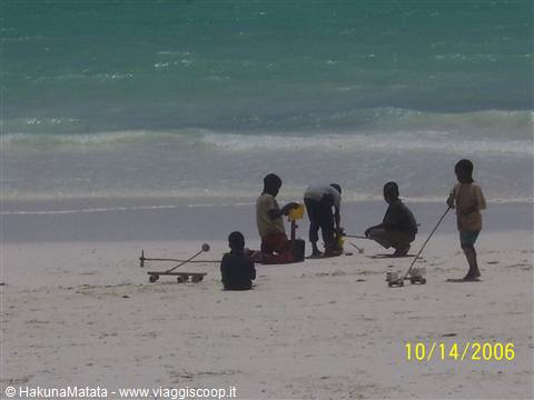 Children play with toy carts on white sand by the turquoise ocean