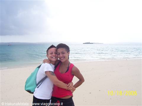 Two girls hugging on a white sand beach, islet in the background