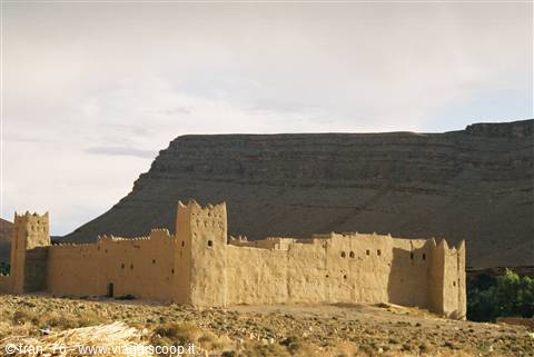 Mud-brick ksar at the foot of a rocky mountain under cloudy sky