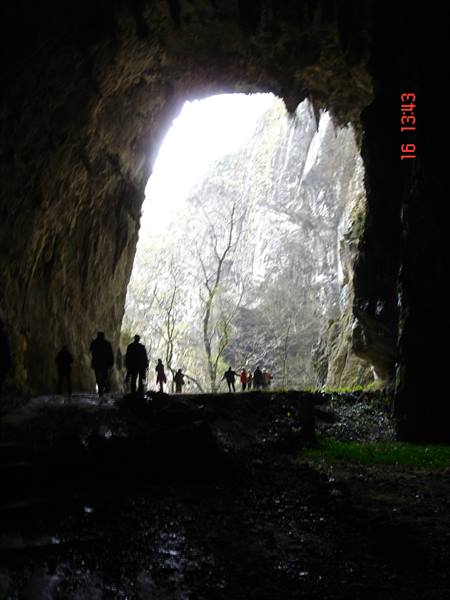 Visitors silhouetted at the entrance of a large limestone cave, daylight outside