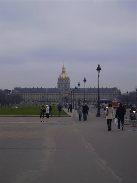 Pedestrians walk toward the Invalides with its golden dome under grey sky