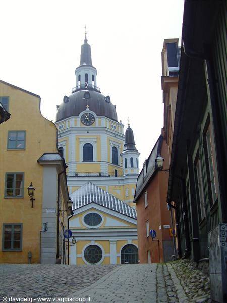 Katarina Church rises over a cobbled street between colorful old houses in Stockholm