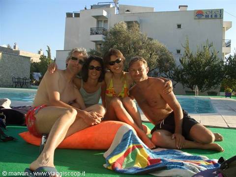Four friends in swimwear sitting by the pool in front of the Mert hotel