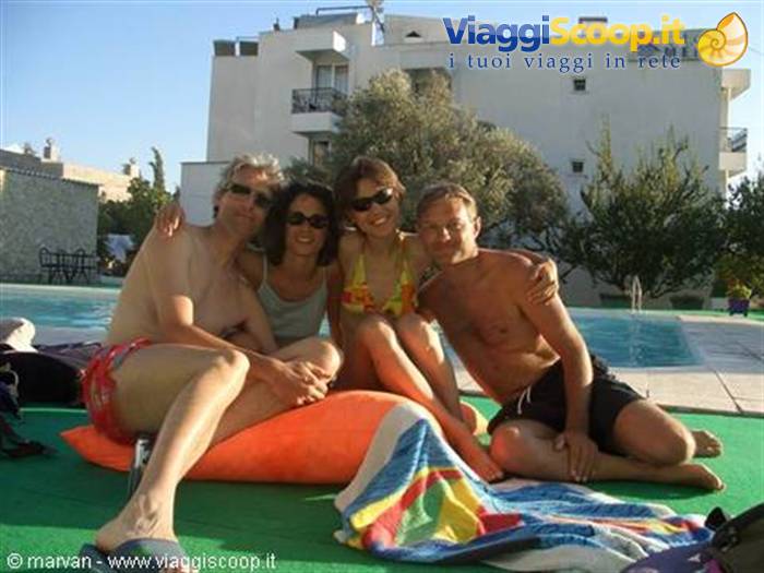 Four friends in swimwear sitting by the pool in front of the Mert hotel