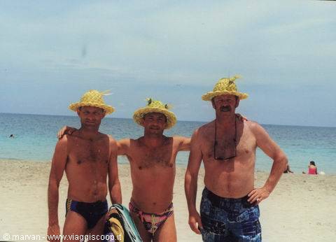 Three shirtless men in straw hats and swimsuits on sandy beach