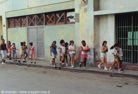Children walking along a weathered wall on a Havana street