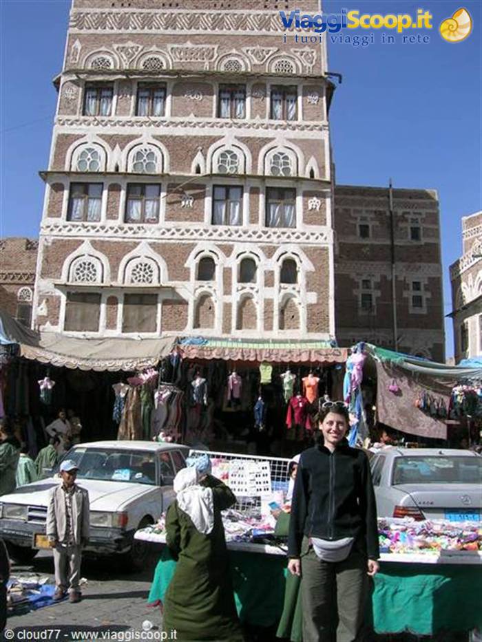 Smiling traveler at Sana'a old market, in front of decorated brick tower house