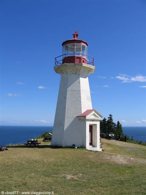 White lighthouse with red lantern on grassy cliff, Cape Enrage